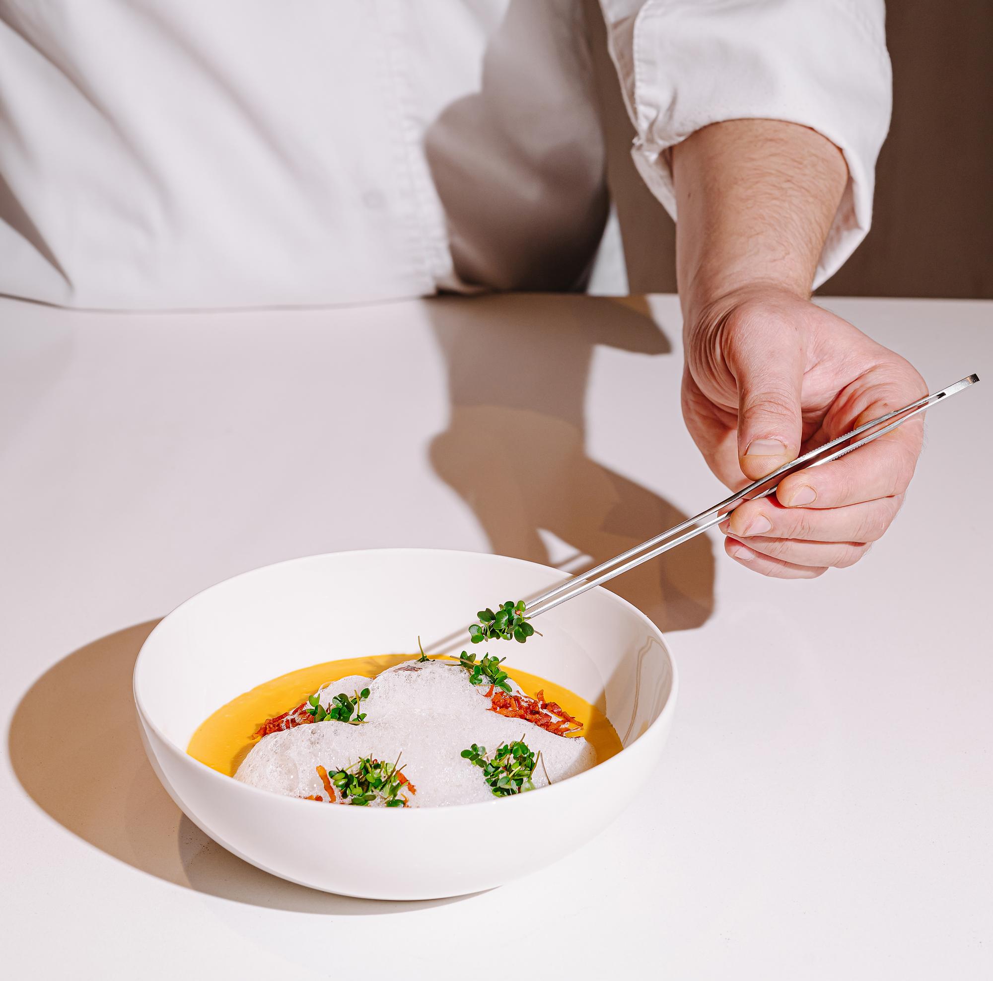 chef arranging plated dish on white table